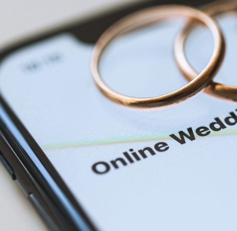 Two golden wedding rings on top of a smartphone and the text on the screen - Online Wedding